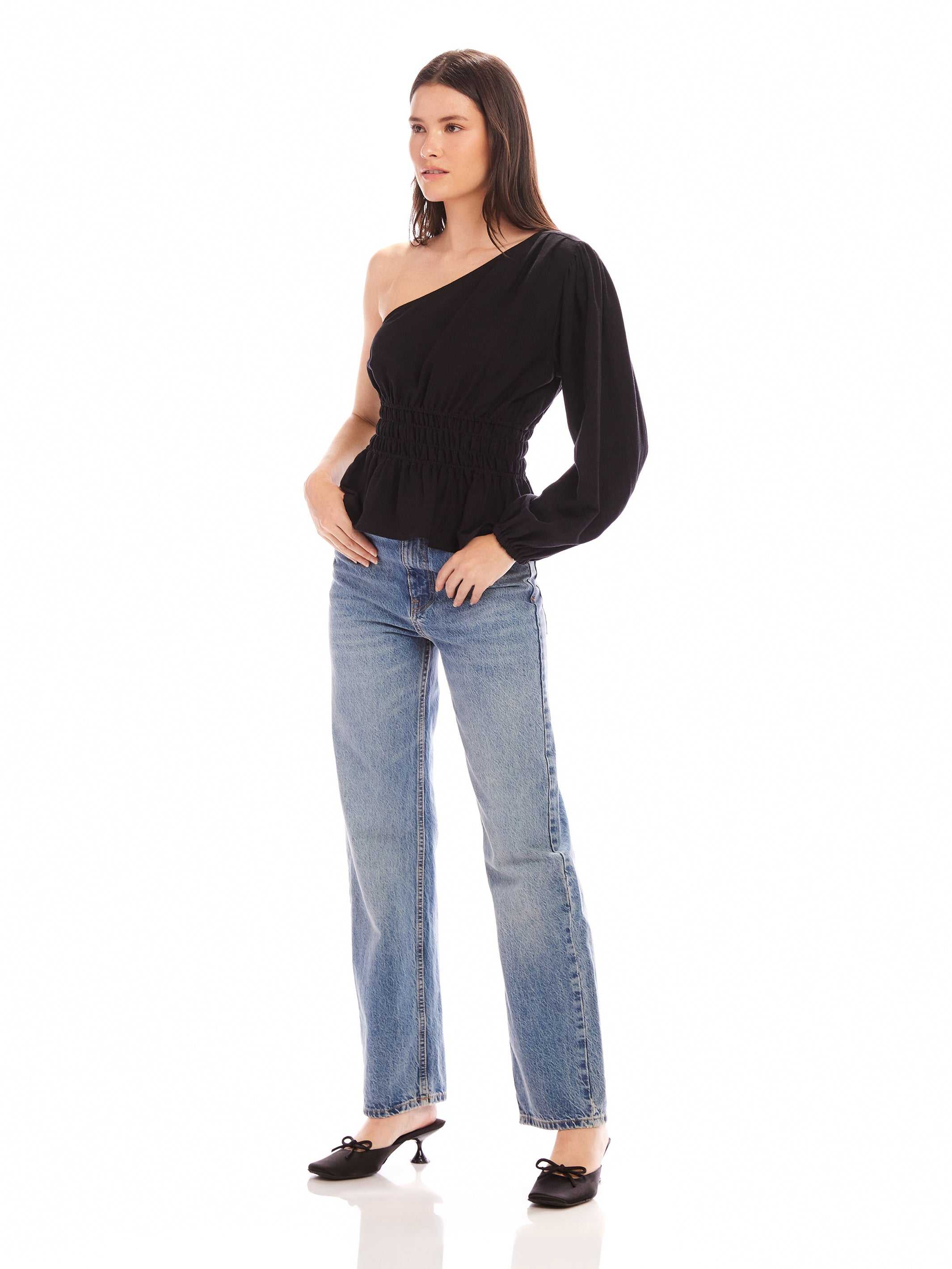 Woman wearing black Talia One-Shoulder Top with elasticized waist and peplum hem paired with blue jeans and black heels