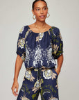 Kasey Peasant Top in navy woven fabric with cream floral vines and green accents, featuring a gathered scoop neck and short sleeves.