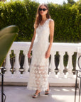 Woman wearing a sleeveless white Kelsie Crochet Dress with floral pattern and scoop neckline, standing outdoors on a balcony.