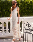Woman wearing a white sleeveless Kelsie Crochet Dress with floral design and scoop neckline standing outdoors by a railing