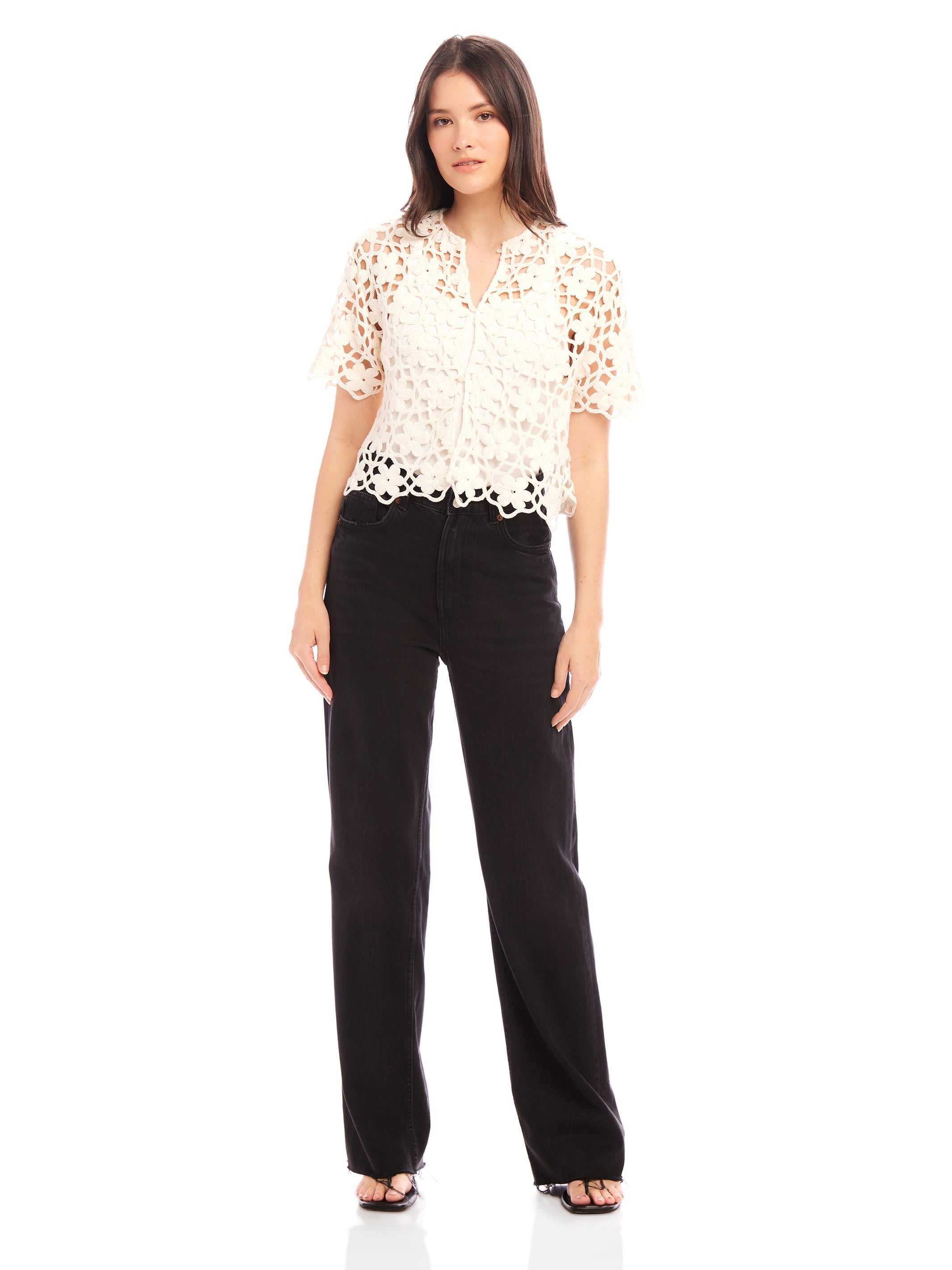 Woman wearing Kamille Crochet Shirt with short sleeves and scalloped hem paired with black pants