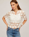 White Kamille Crochet Shirt with floral pattern, short sleeves, front button closure, and scalloped hem, worn with jeans.