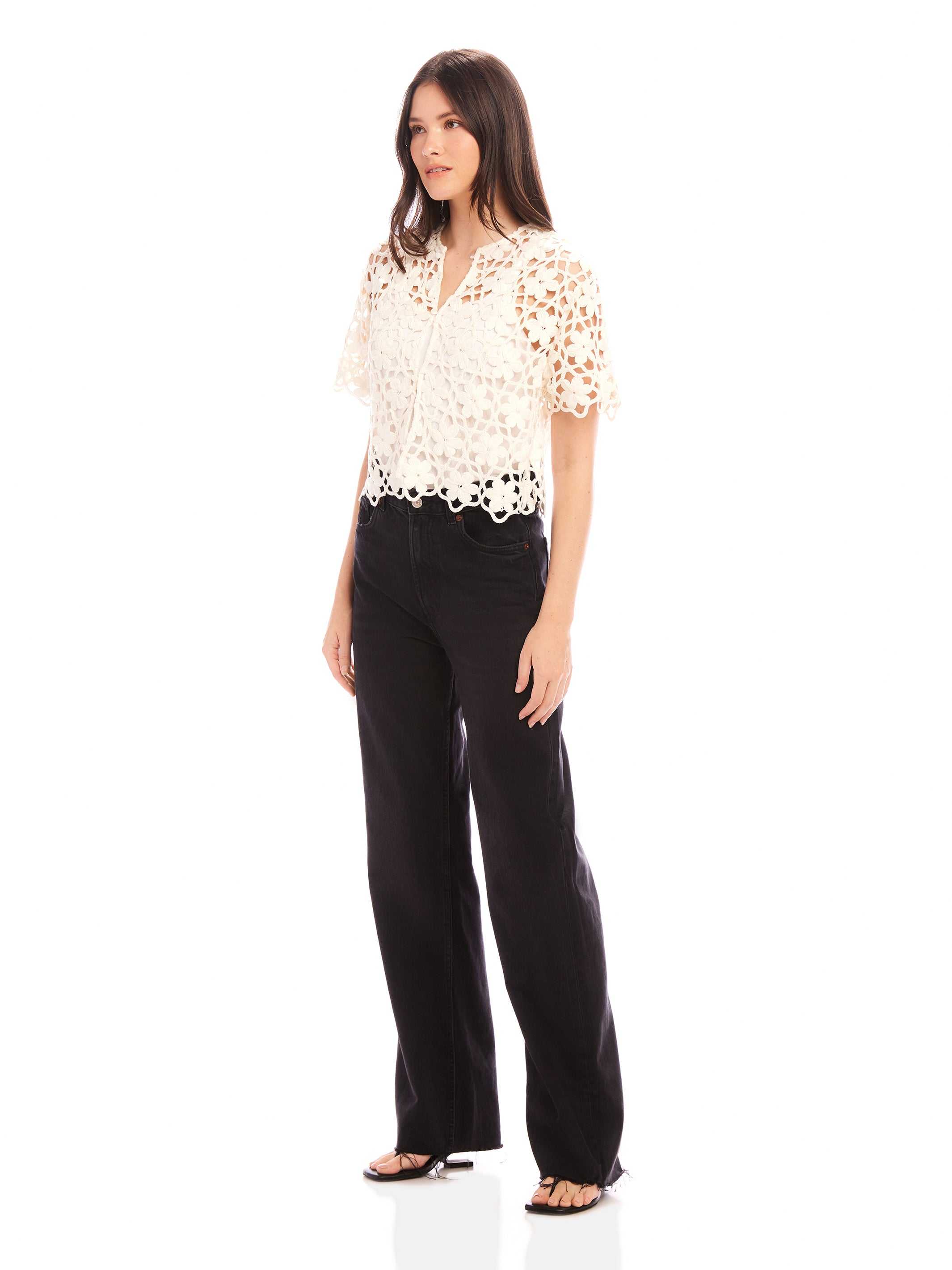 Woman wearing Kamille Crochet Shirt with short sleeves and scalloped hem, paired with black pants