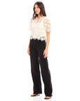 Woman wearing Kamille Crochet Shirt with short sleeves and scalloped hem, paired with black pants
