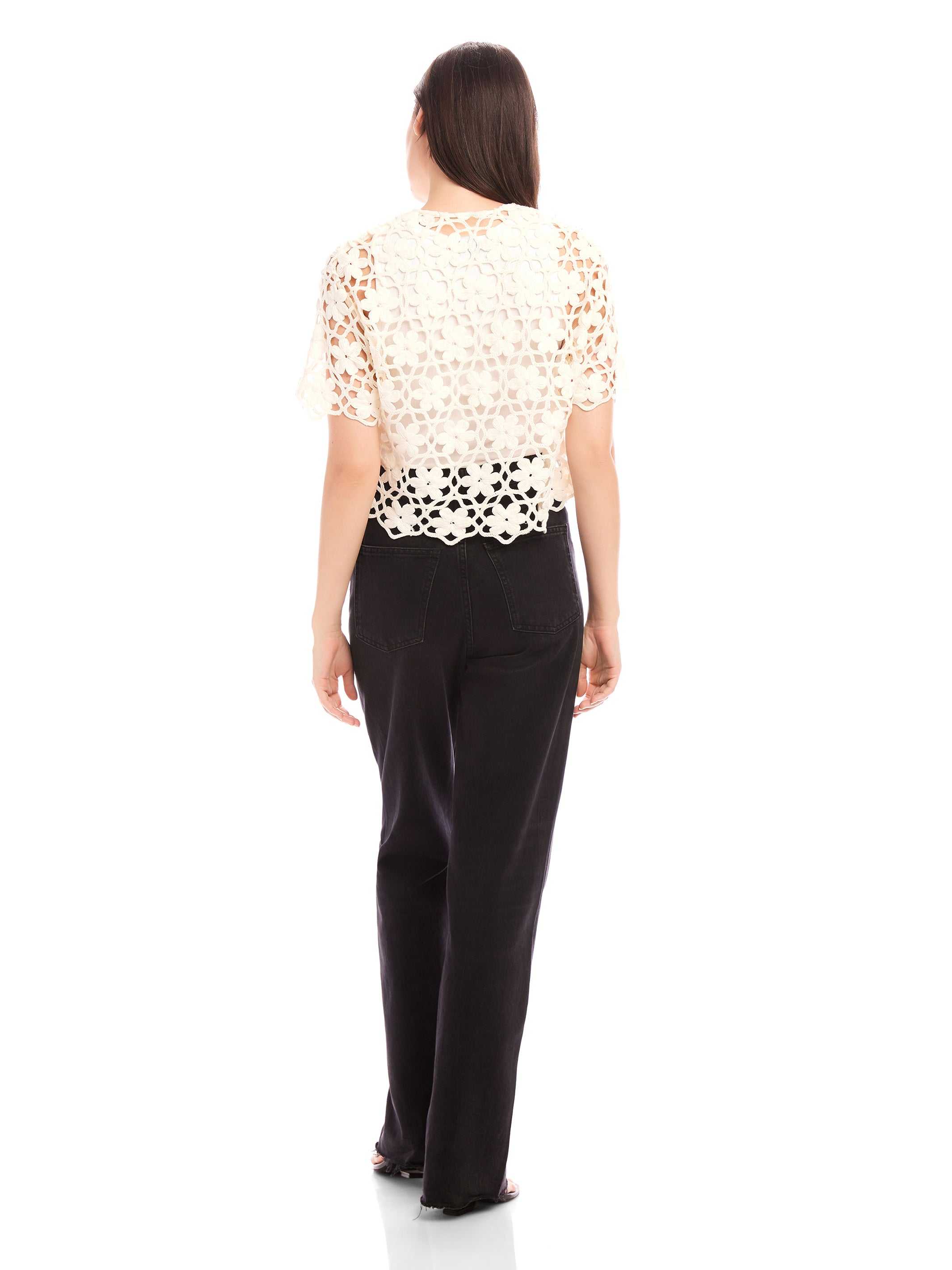 Back view of Kamille Crochet Shirt with floral pattern, short sleeves, scalloped hem, worn with black pants