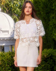 White Kamille Crochet Shirt with short sleeves, button front, and scalloped hem worn over a white tank top