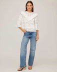 Woman wearing white Flora Eyelet Lace Top with embroidered floral eyelet design and ruffle trim, paired with blue jeans and heels.