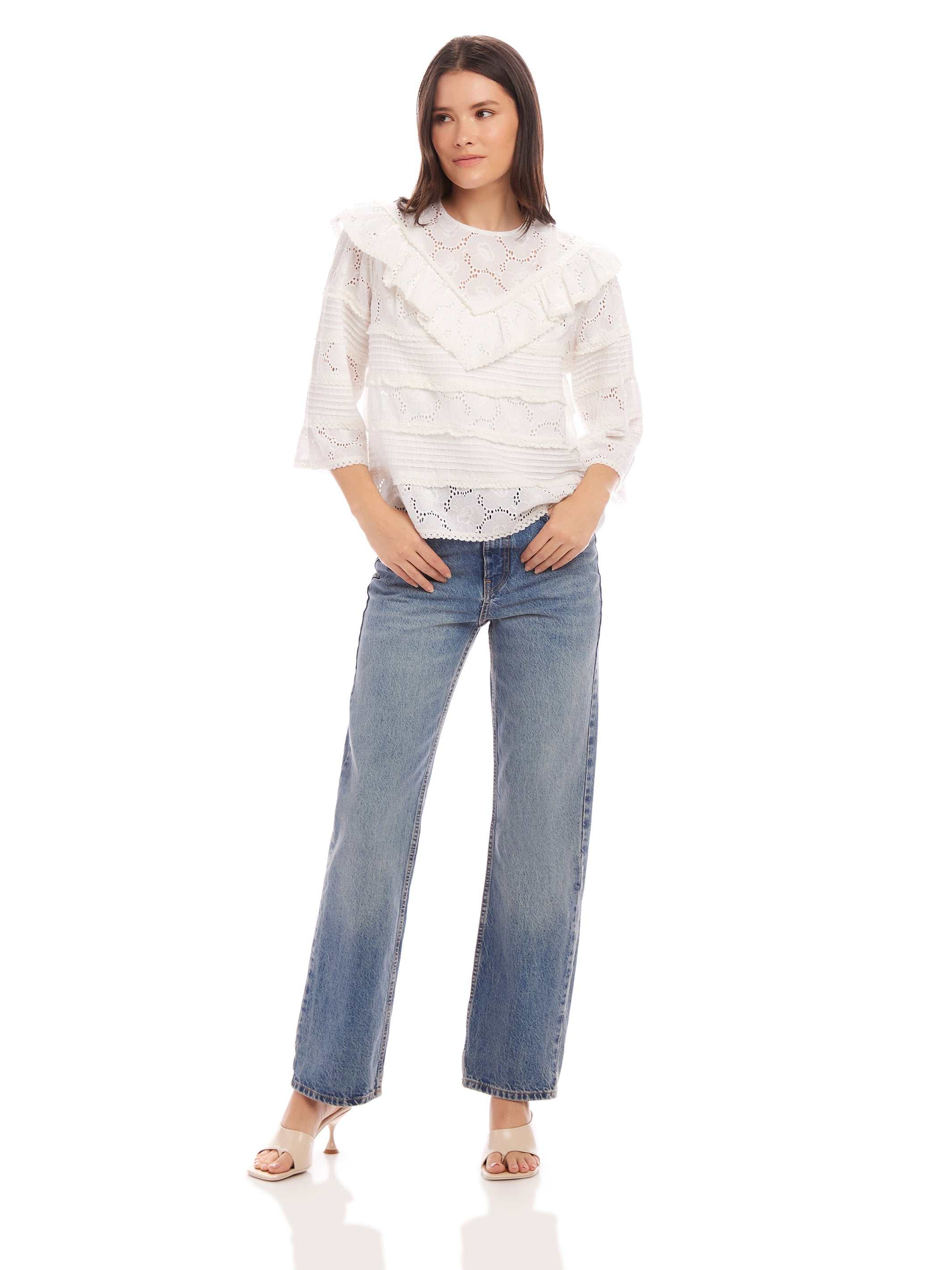 Woman wearing Flora Eyelet Lace Top with floral embroidered eyelet design, ruffle trim, elbow sleeves, and crew neck paired with blue jeans.