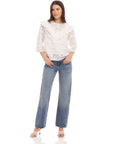 Woman wearing Flora Eyelet Lace Top with floral embroidered eyelet design, ruffle trim, elbow sleeves, and crew neck paired with blue jeans.