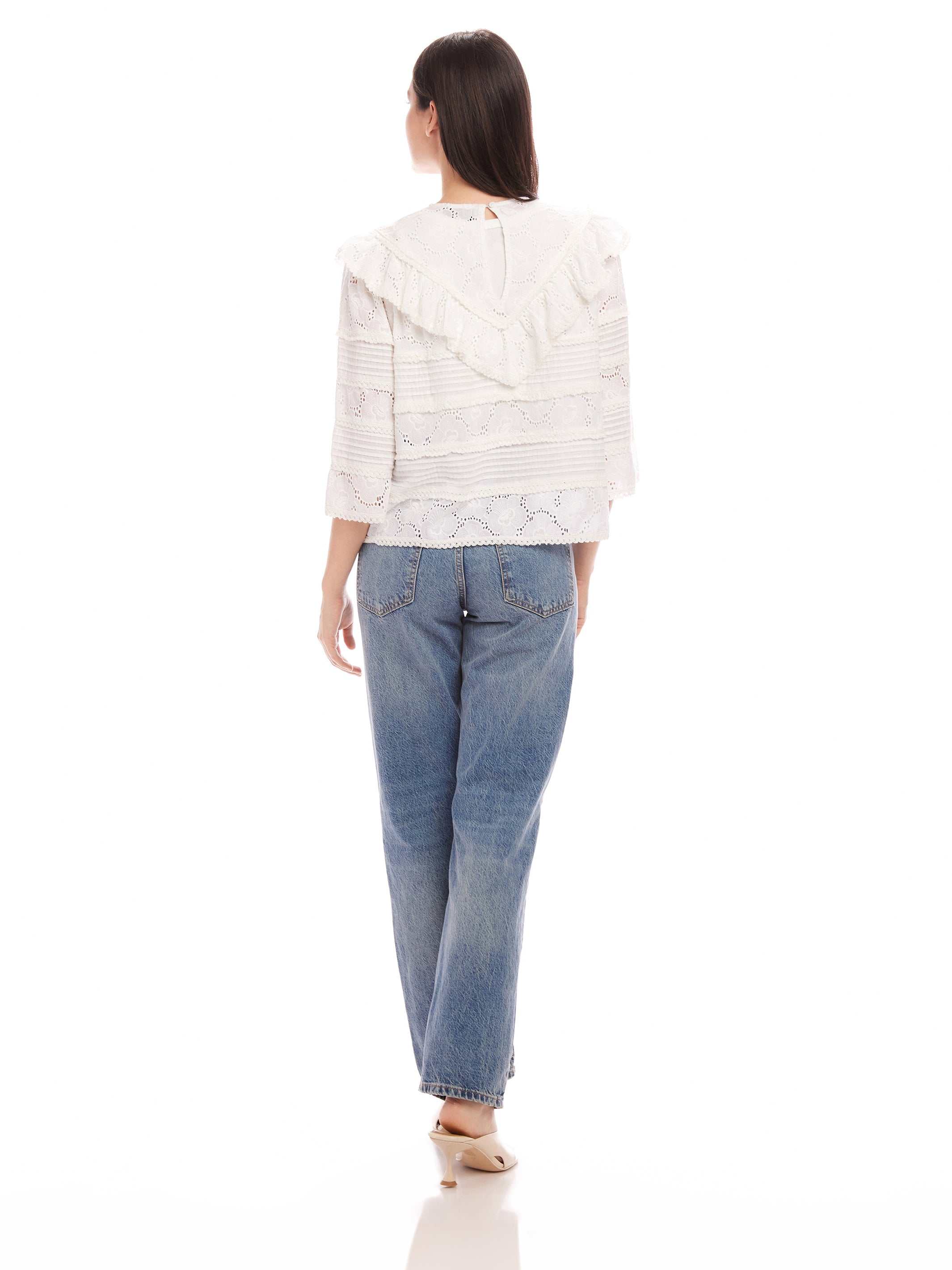 Woman wearing Flora Eyelet Lace Top with floral eyelet design and ruffle trim, paired with blue jeans, shown from back.