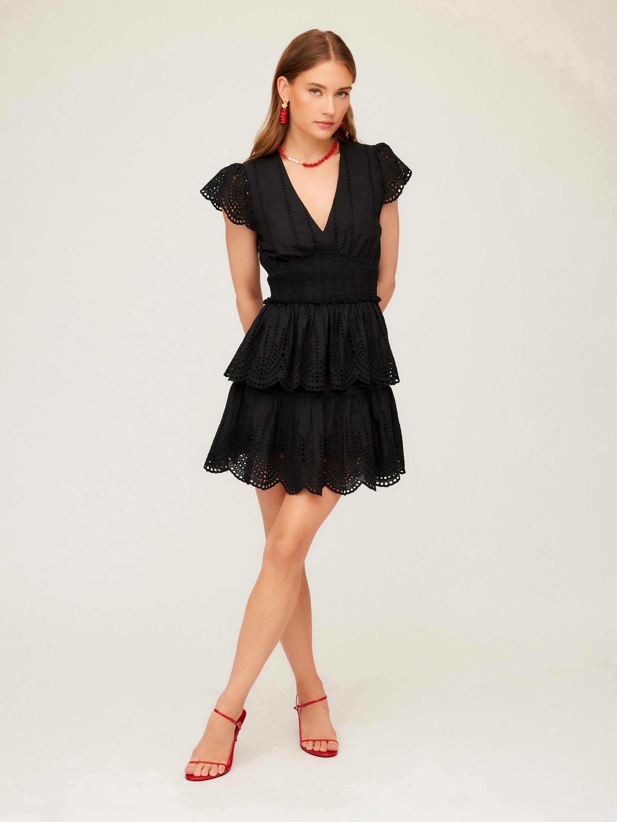 Woman wearing black Isla embroidered tiered dress with cap sleeves and V-neck paired with red heels and accessories