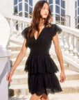 Woman wearing black Isla Embroidered Tiered Dress with fitted waist, cap sleeves, V-neck, and tiered eyelet design outdoors on stairs