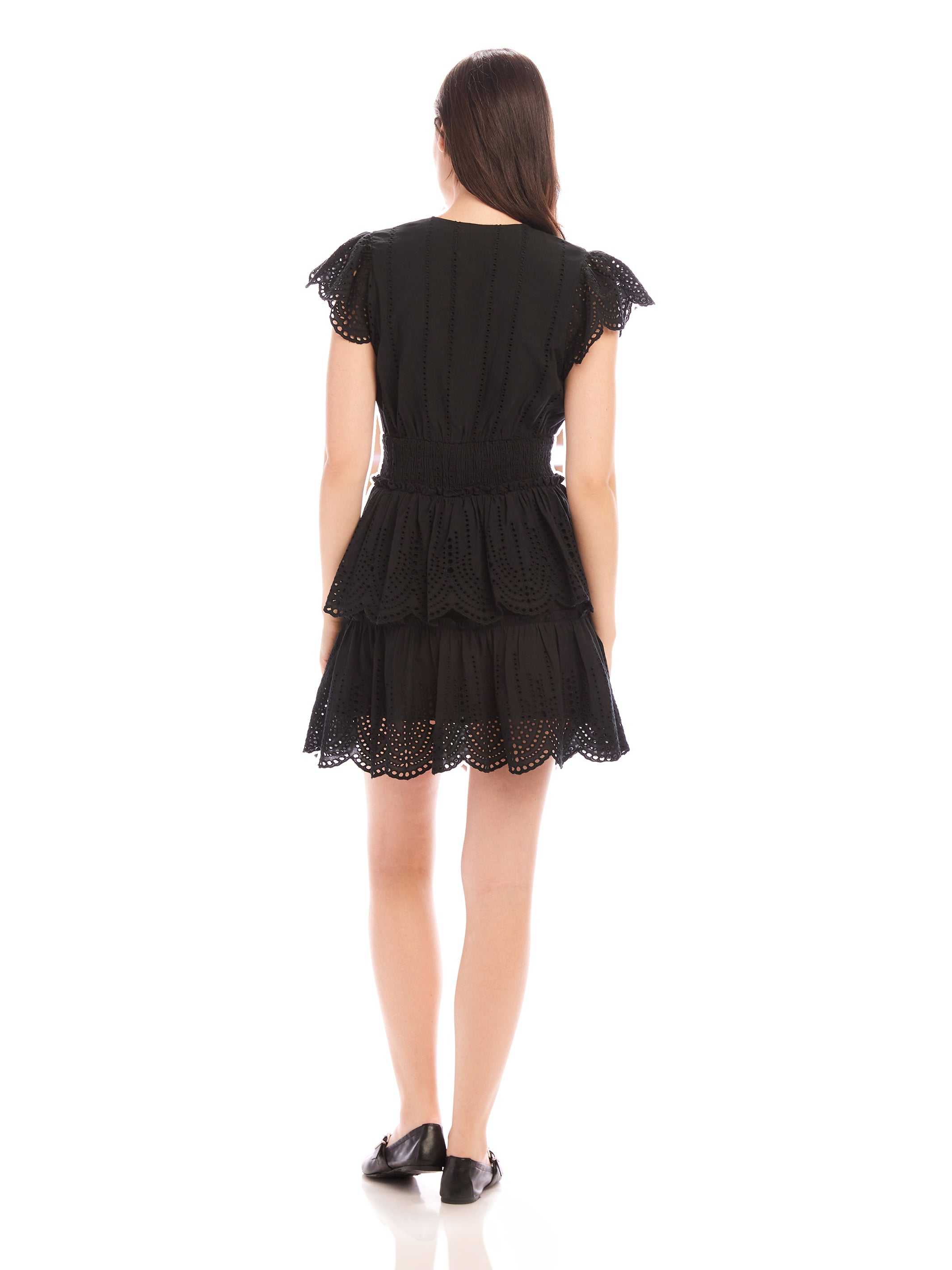 Back view of a woman wearing a black Isla Embroidered Tiered Dress with cap sleeves and tiered skirt
