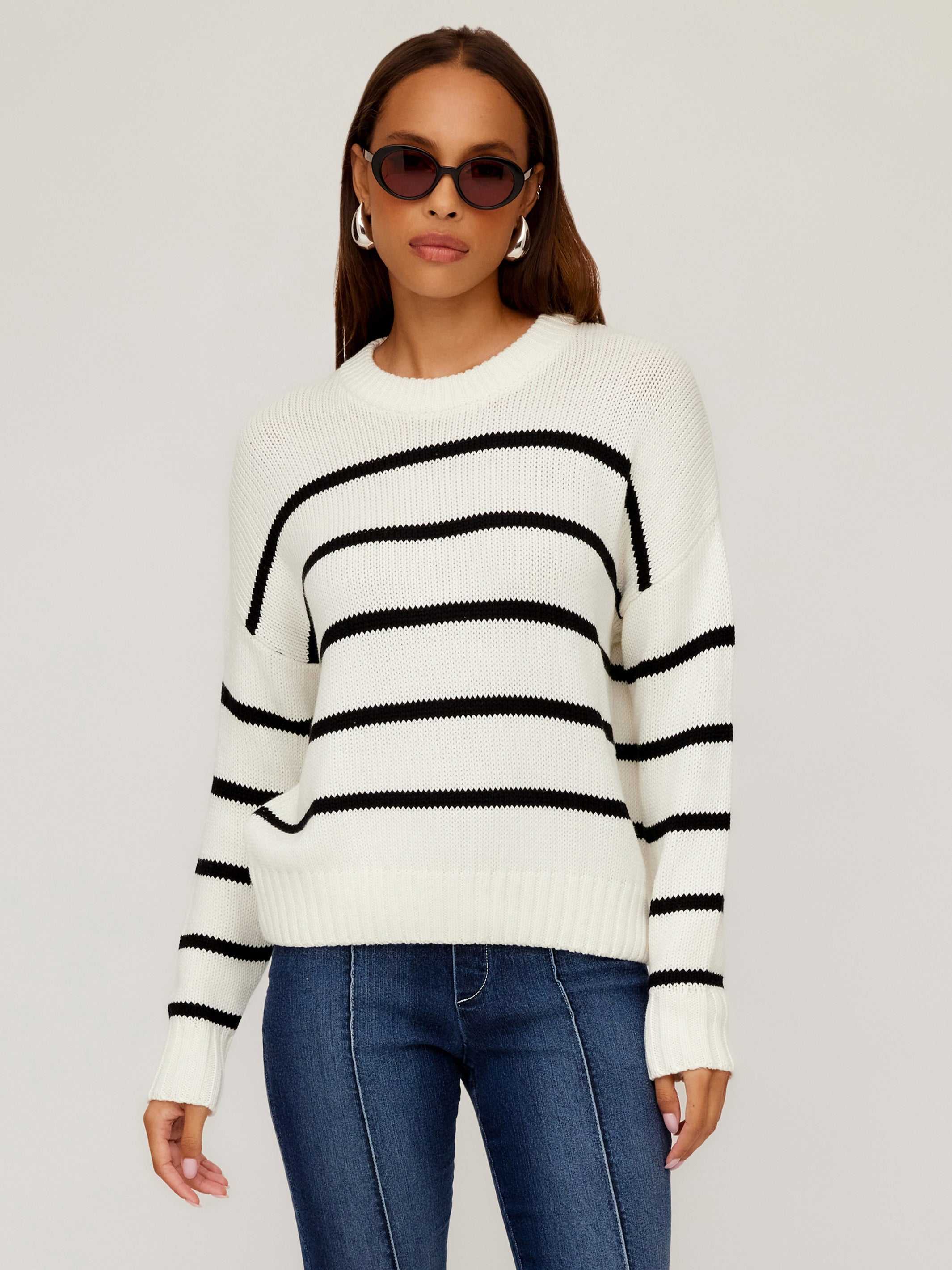 Woman wearing a white Luca Crewneck Sweater with black horizontal stripes and ribbed details paired with blue jeans