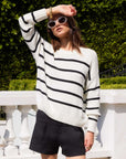 Woman wearing a white Luca Crewneck Sweater with black stripes and ribbed detail, paired with black shorts outdoors