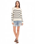 Woman wearing a white Luca Crewneck Sweater with black stripes, paired with denim shorts and sandals.