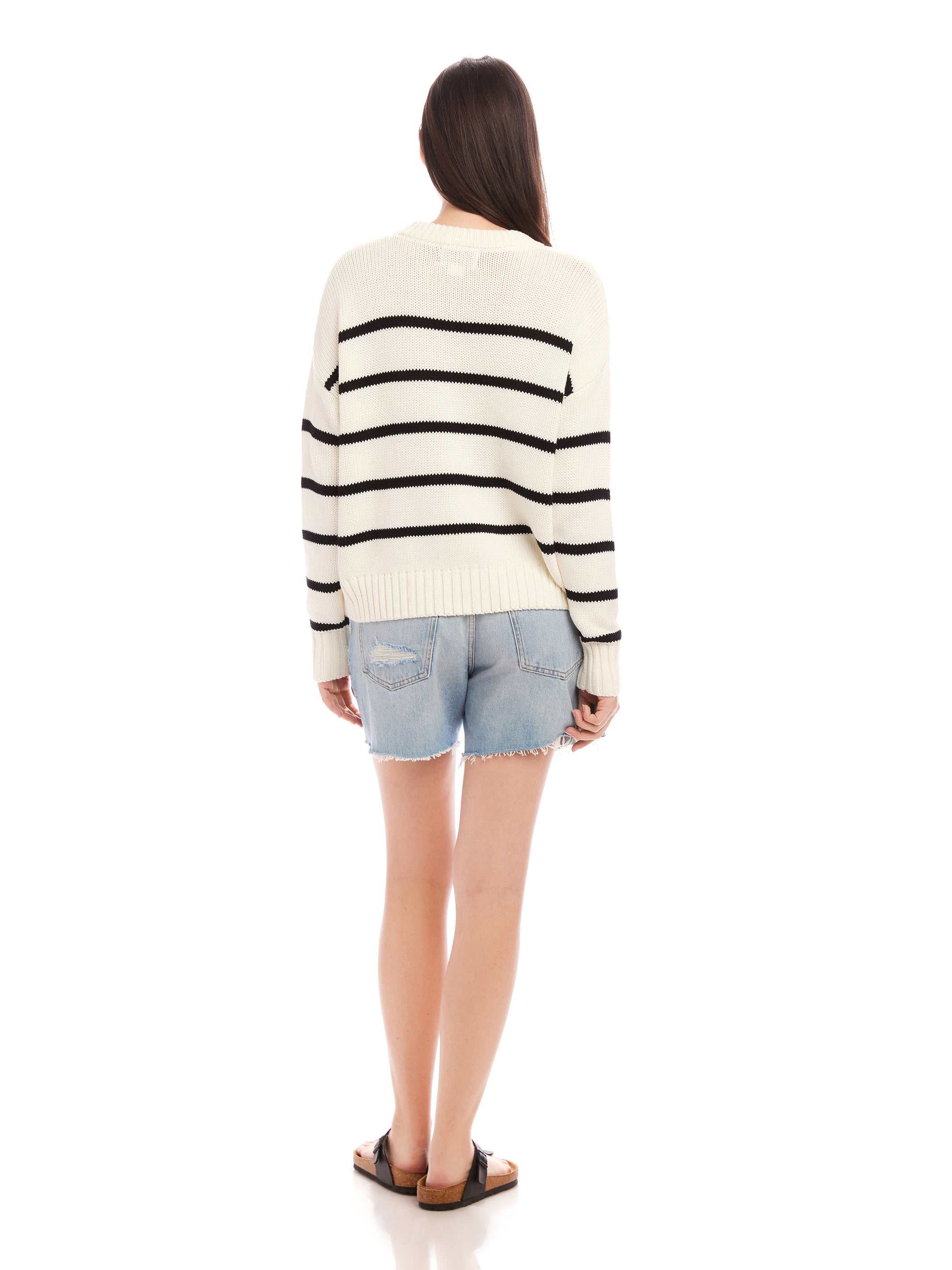 Back view of a woman wearing a white Luca Crewneck Sweater with black stripes and light denim shorts