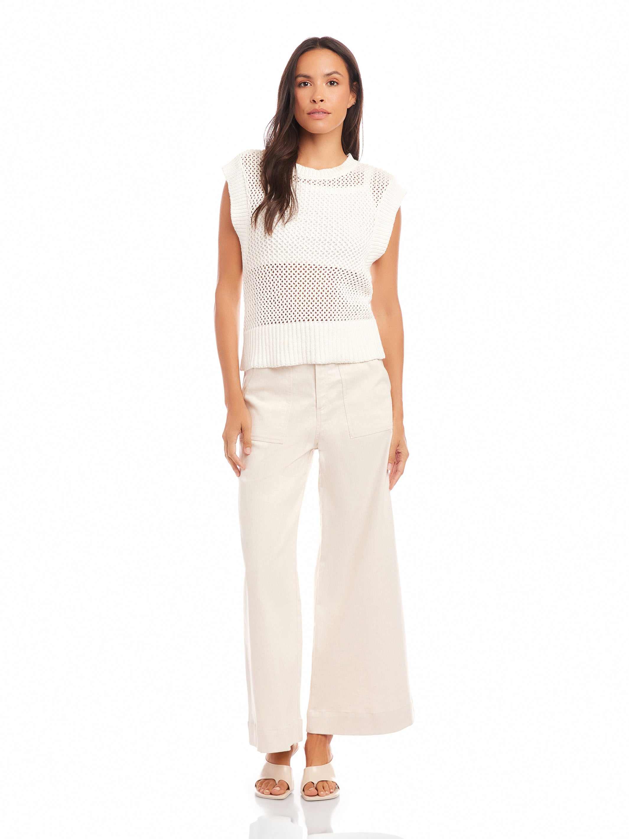 Woman wearing a white Carly Sleeveless Crochet Top with wide knit pattern, crew neckline, and ribbed hem paired with light-colored wide-leg pants.