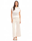 Woman wearing a white Carly Sleeveless Crochet Top with wide knit pattern, crew neckline, and ribbed hem paired with light-colored wide-leg pants.