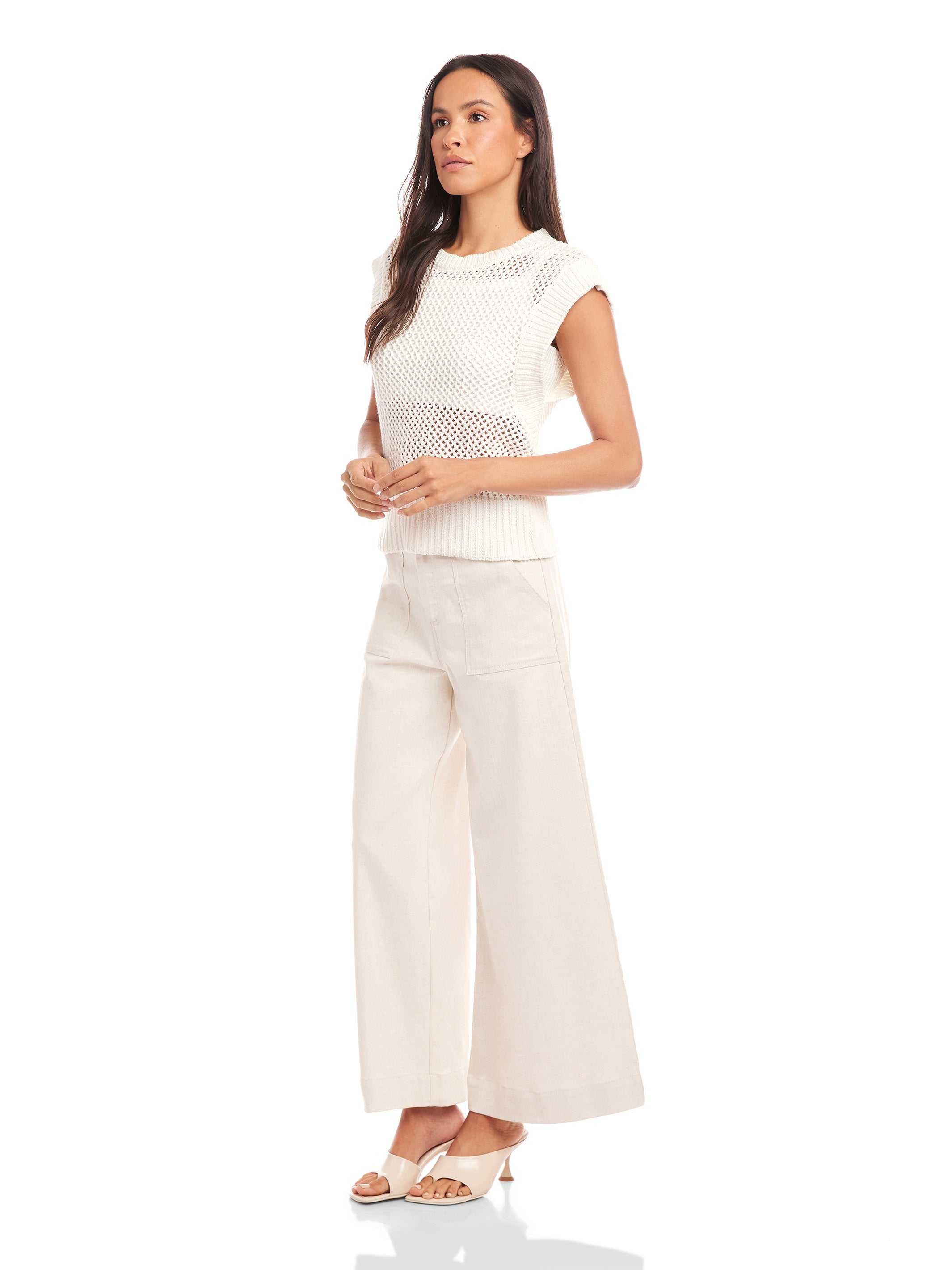 Woman wearing white Carly sleeveless crochet top with wide knit texture, crew neck, and wide ribbed hem, paired with light wide-leg pants and sandals.
