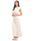 Woman wearing white Carly sleeveless crochet top with wide knit texture, crew neck, and wide ribbed hem, paired with light wide-leg pants and sandals.