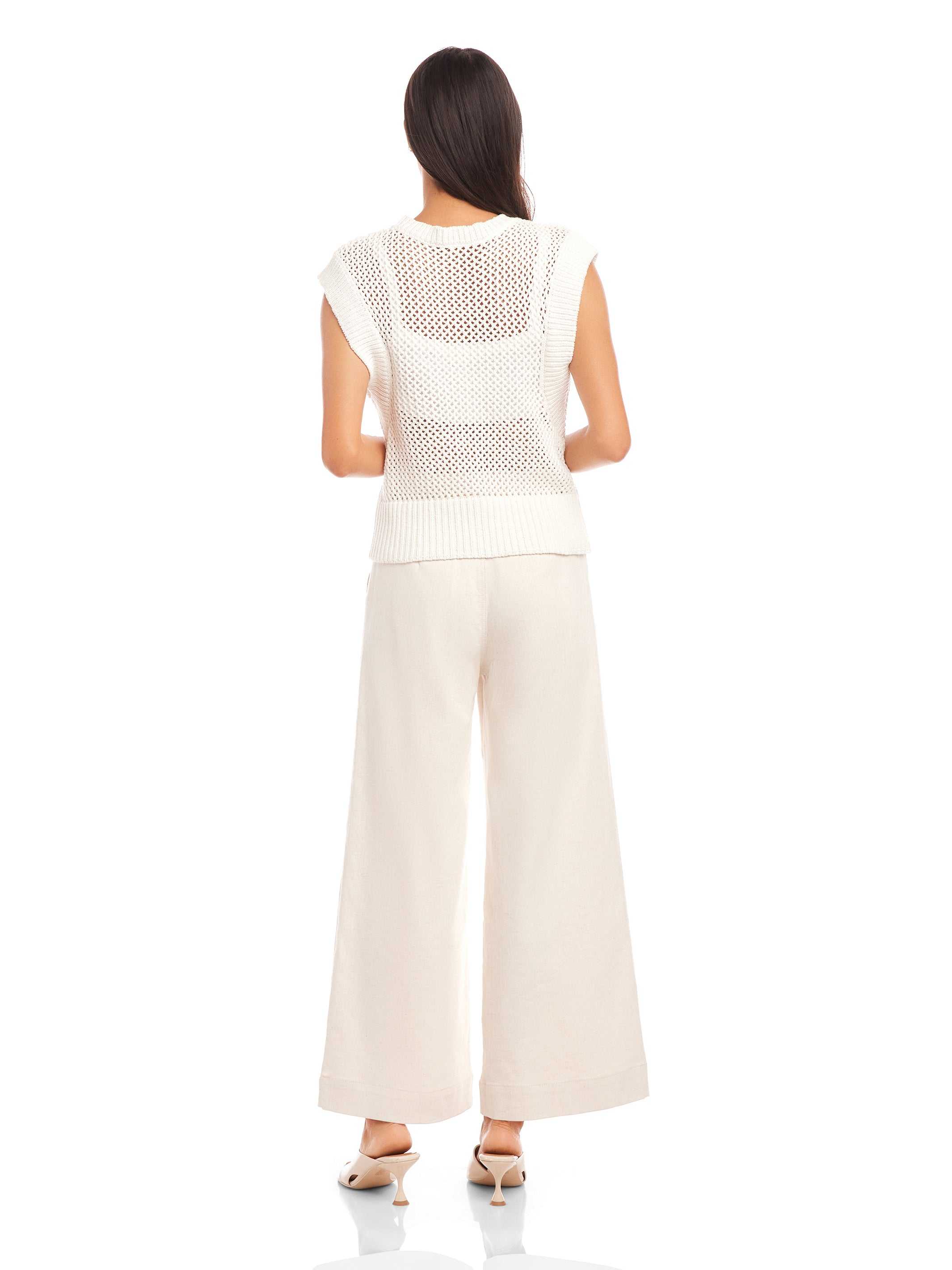back view of woman wearing white Carly sleeveless crochet top with wide knit and crew neck paired with loose white pants