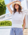 Woman wearing white Carly Sleeveless Crochet Top with crew neck and ribbed hem, paired with striped pants and a wide-brim hat outdoors
