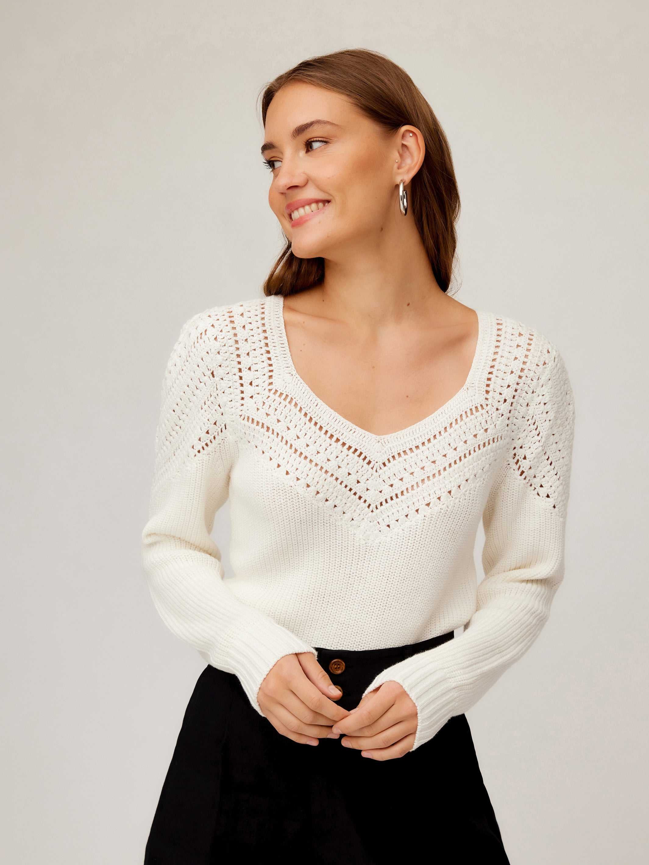 Woman wearing white Lola Crochet Sweater with contrast crochet pattern and V-neckline, paired with black pants