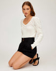 Woman wearing white Lola Crochet Sweater with long sleeves and modified V-neckline paired with black shorts and sandals