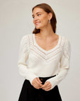 Woman wearing white Lola Crochet Sweater with contrast crochet pattern and V-neckline, paired with black pants