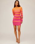 Woman wearing Naya Variegated Stripe Dress with long bell sleeves and fitted mini silhouette in pink and orange tones