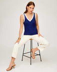 Woman wearing a navy blue sleeveless Nicole Sweater Tank with a V-neckline and wide ribbed detail, paired with white pants and sandals.