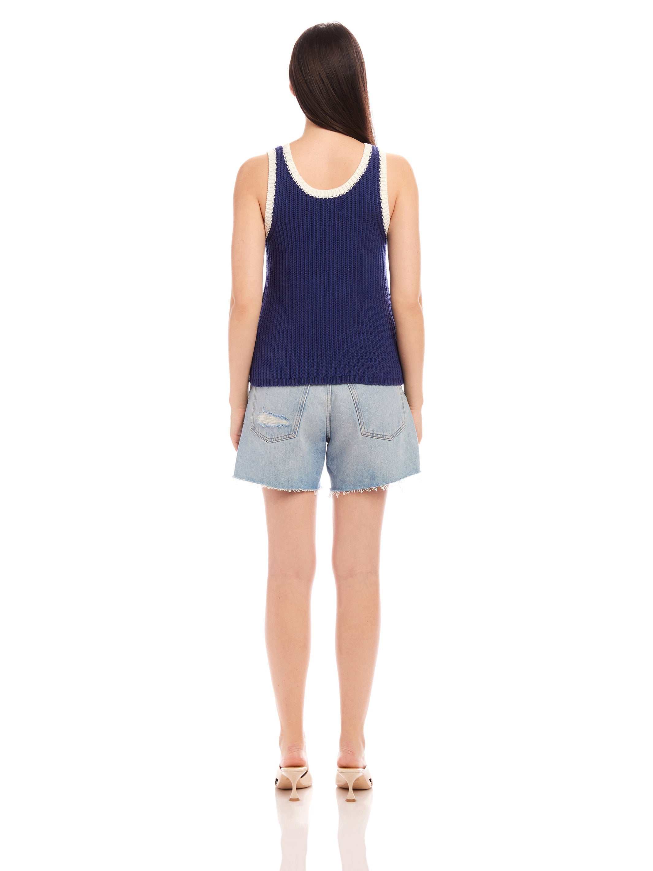 Woman wearing navy Nicole Sweater Tank with white ribbed trim and light denim shorts, shown from the back.