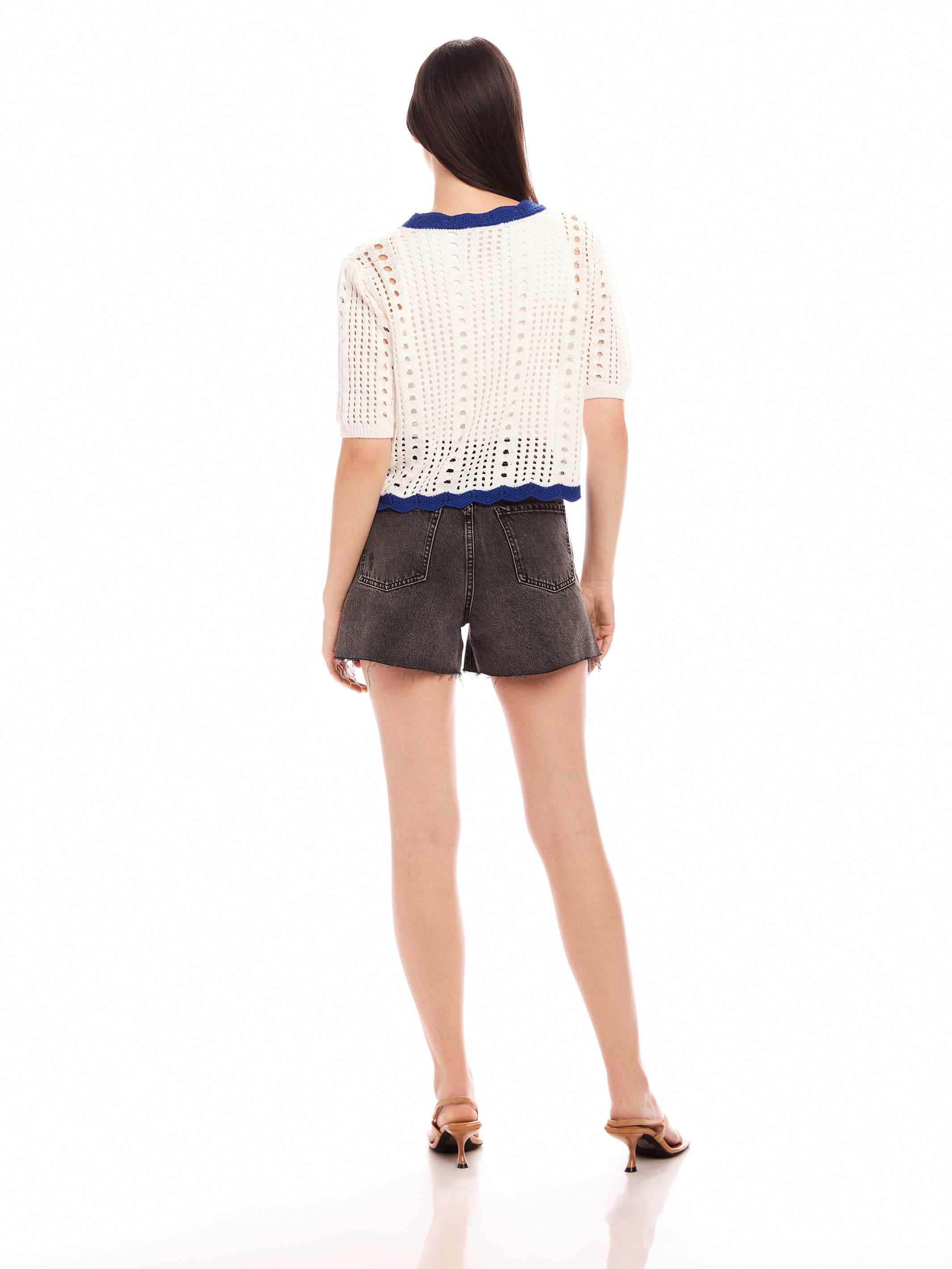 Woman wearing white Betsy Crochet Top with scalloped hem and short sleeves, paired with black shorts and heels, shown from back.