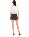 Woman wearing white Betsy Crochet Top with scalloped hem and short sleeves, paired with black shorts and heels, shown from back.