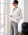 Woman wearing white Cely Cropped Cardigan with long raglan sleeves and plaid high-waisted pants indoors by window