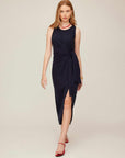 Woman wearing a sleeveless navy Maddie Side-Knot Midi Dress with side slit and crew neck, styled with red sandals and necklace.