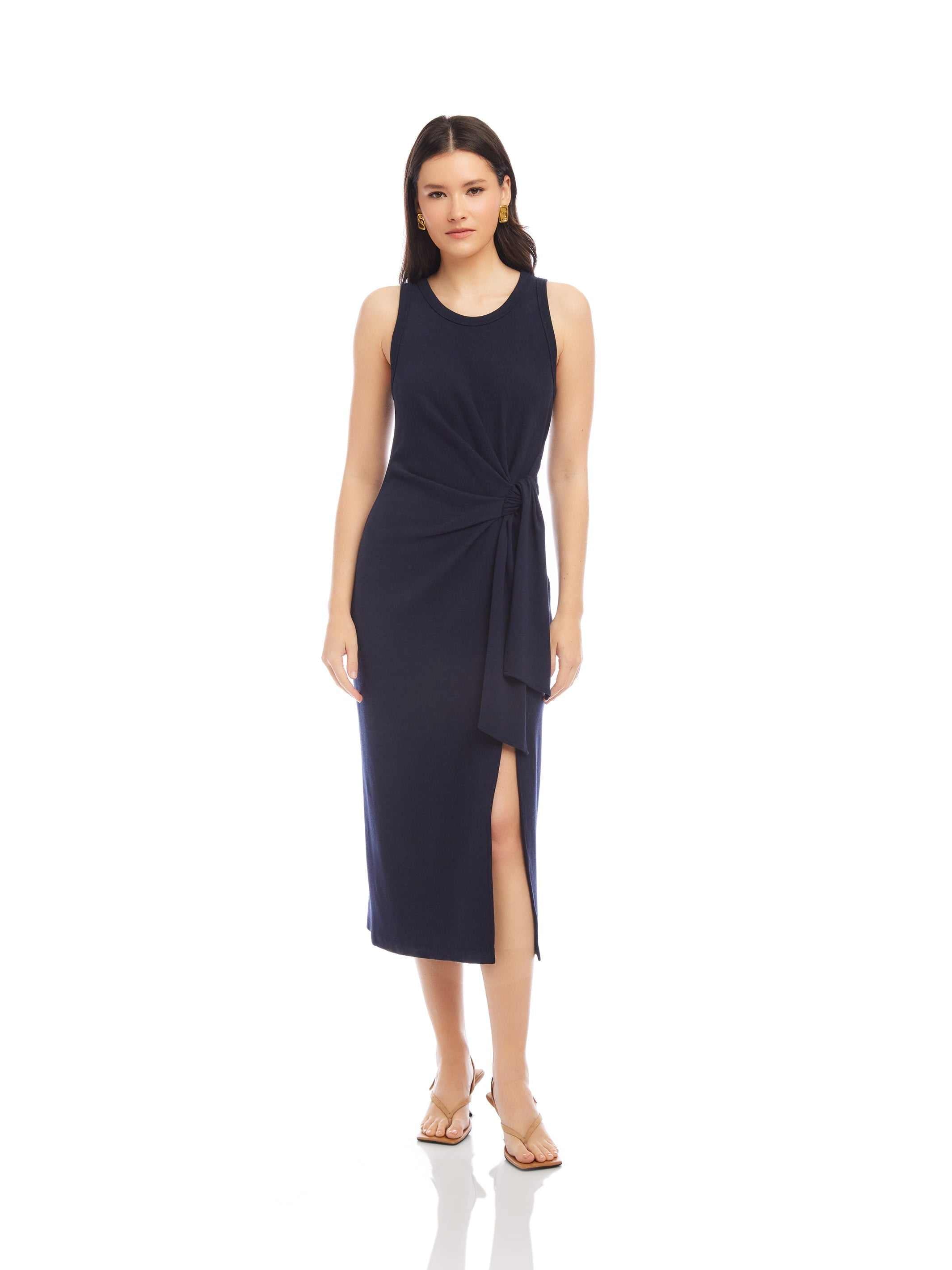 Woman wearing a sleeveless navy Maddie Side-Knot Midi Dress with a side knot detail and slit.