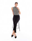 Woman wearing Sigourney Pintuck Pants with a striped sleeveless top and black pointed shoes sitting on a stool.