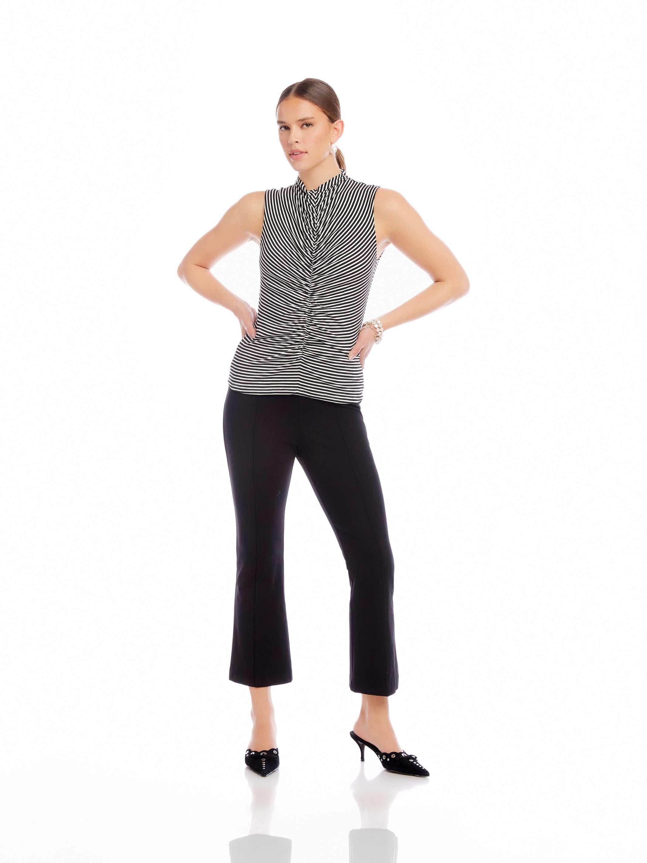 woman wearing black high-rise wide leg Sigourney Pintuck Pants with elastic waist and cropped length, paired with sleeveless striped top and black heels on white background