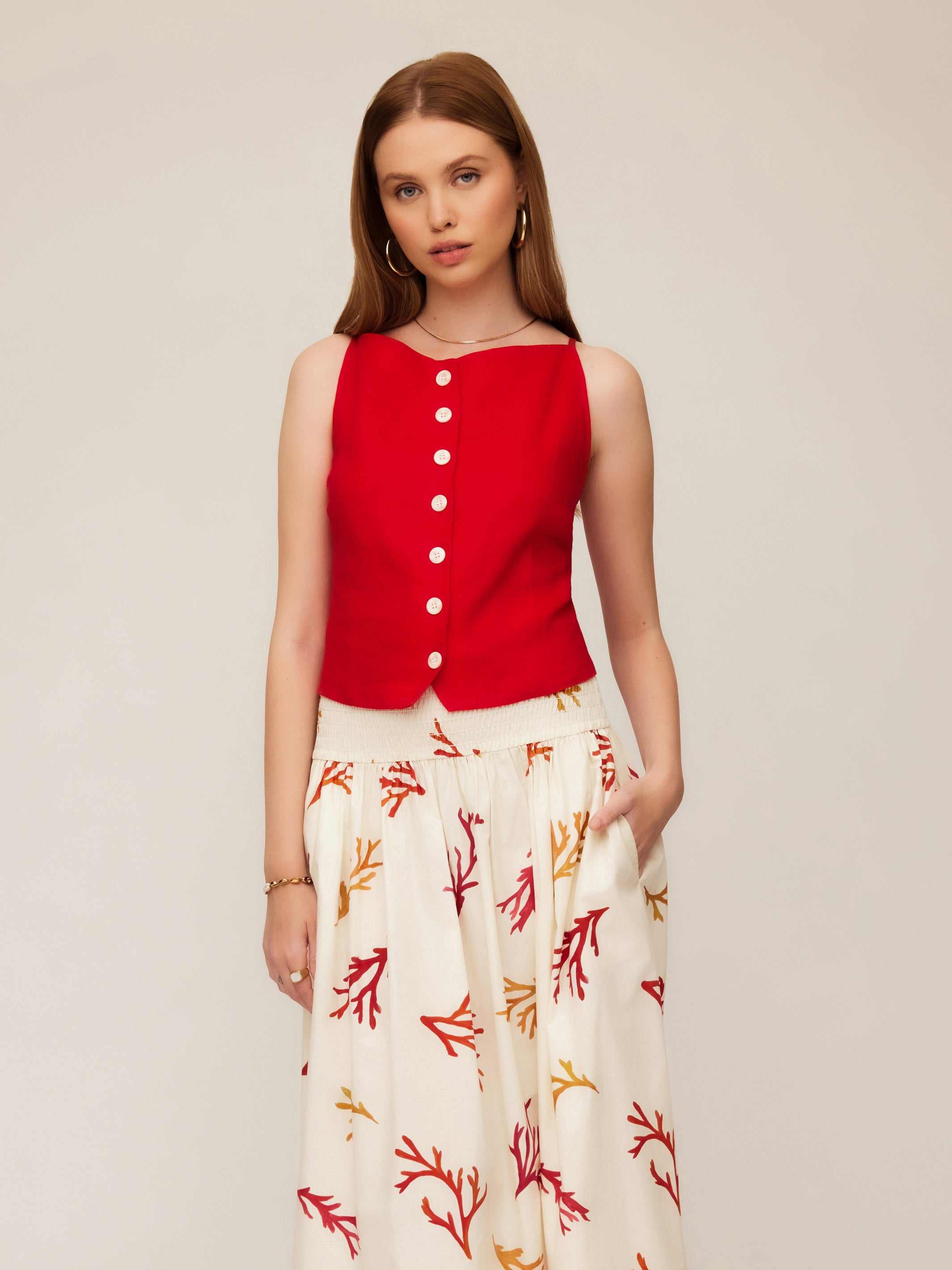 Woman wearing red Elis sleeveless button-up top with white functional buttons and patterned wide-leg pants.