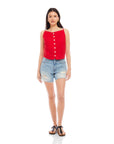 Woman wearing red Elis sleeveless button-up linen top with button details and distressed denim shorts.