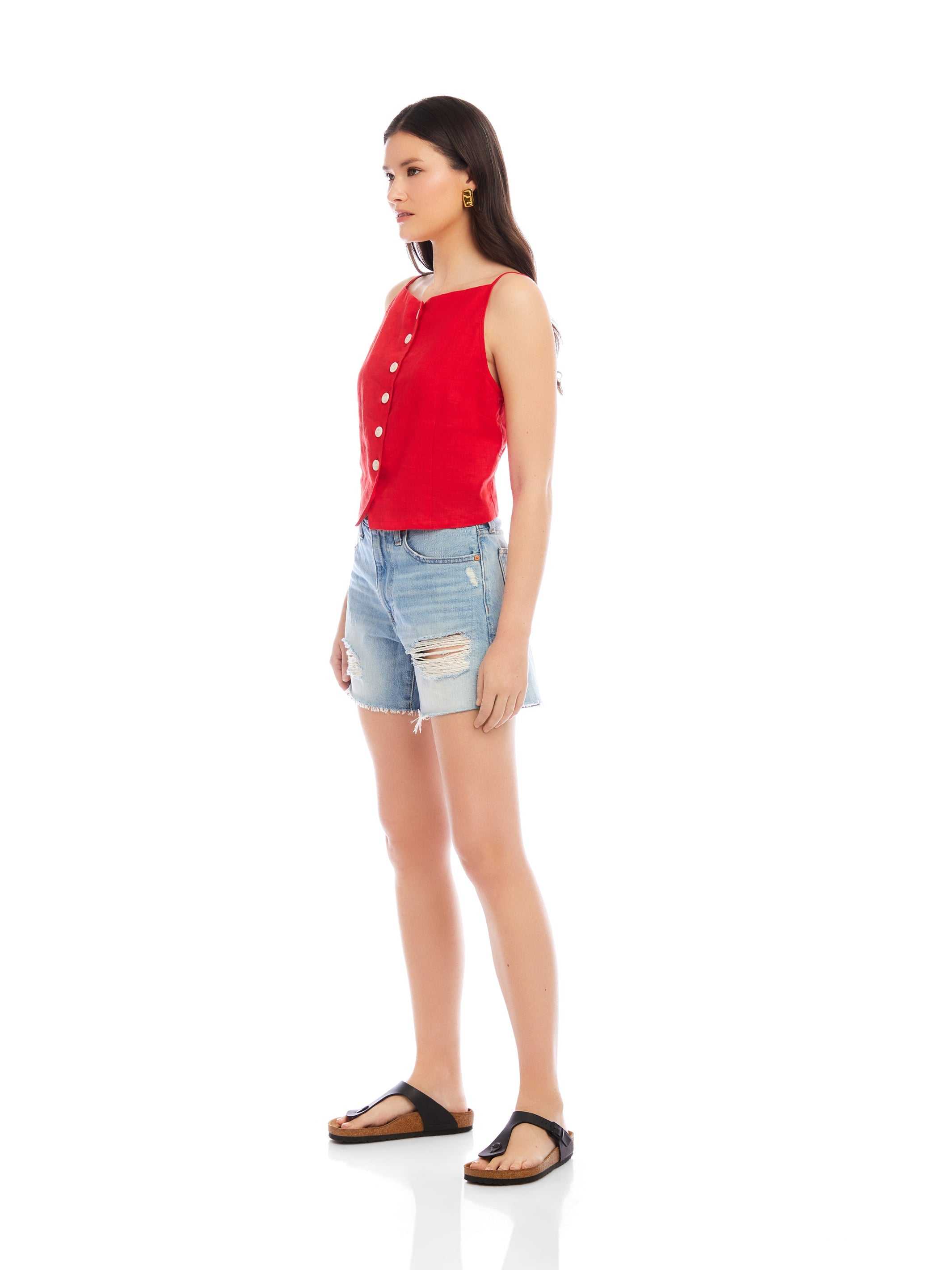 Model wearing red Elis sleeveless button-up top with boxy fit paired with distressed denim shorts and black sandals