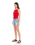Model wearing red Elis sleeveless button-up top with boxy fit paired with distressed denim shorts and black sandals