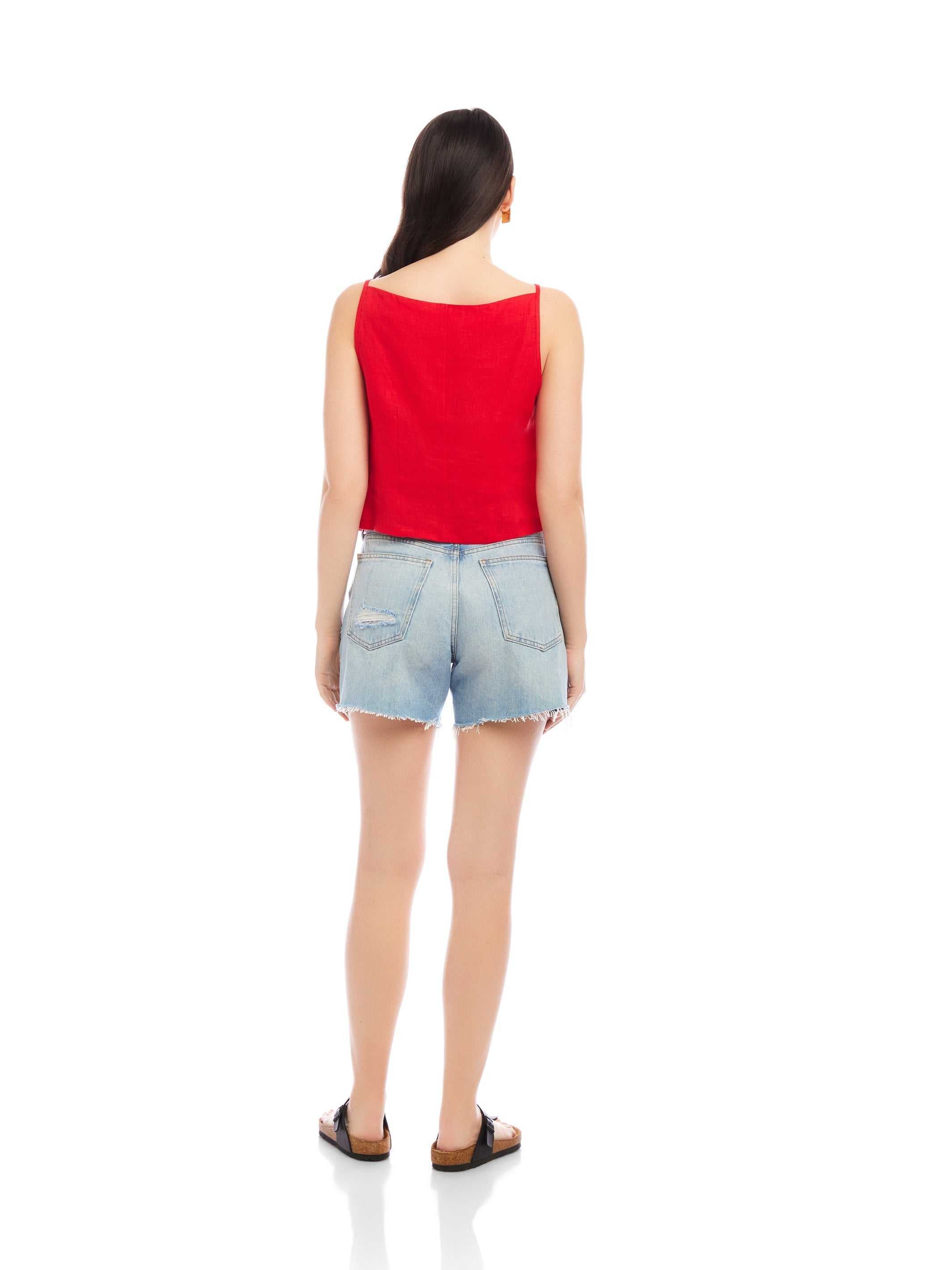 woman wearing red Elis sleeveless button-up top with boxy fit and light blue denim shorts back view