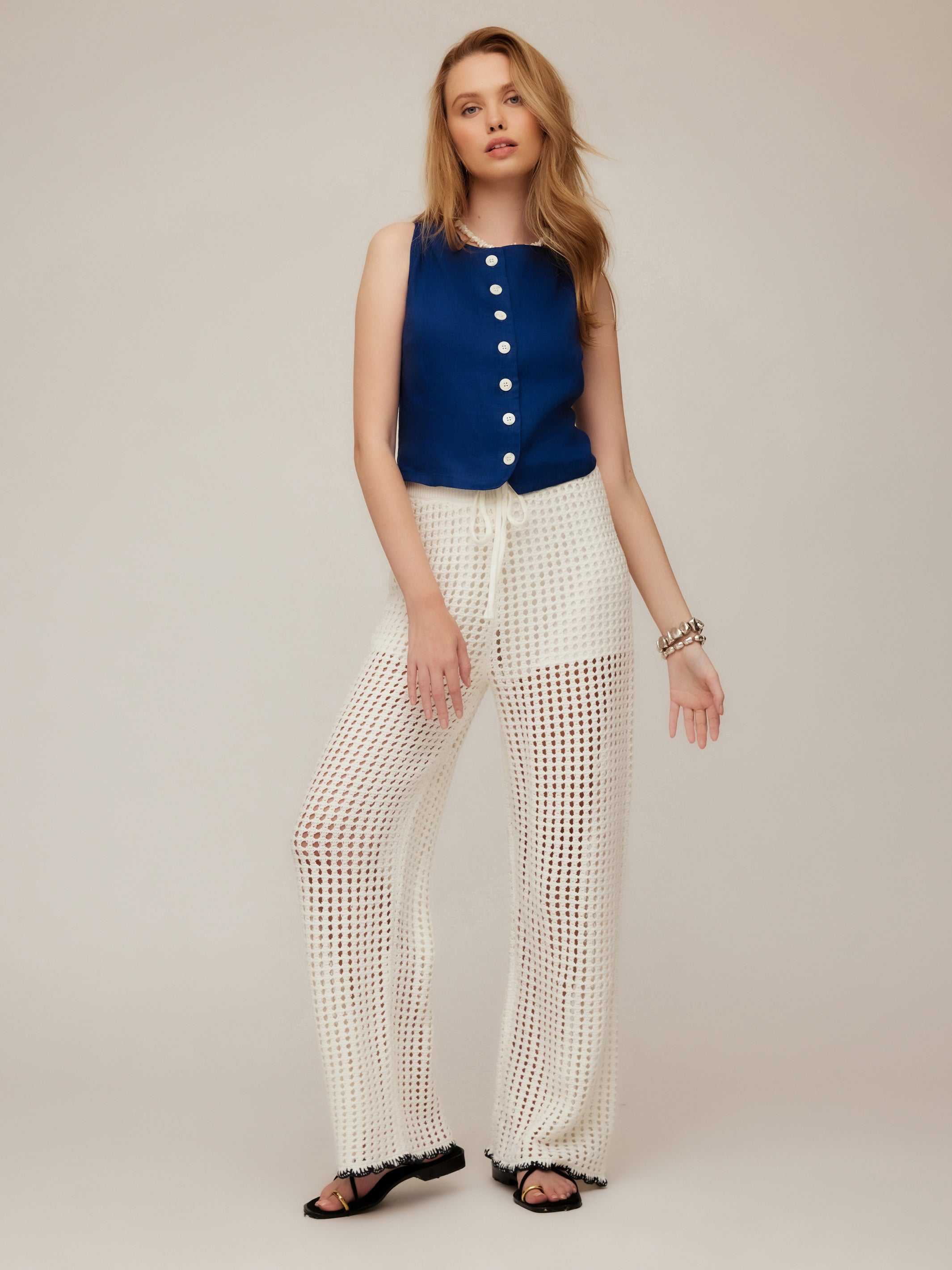 Woman wearing Elis sleeveless button-up top in navy with white wide-leg crochet pants.