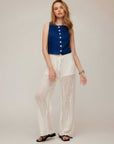 Woman wearing Elis sleeveless button-up top in navy with white wide-leg crochet pants.