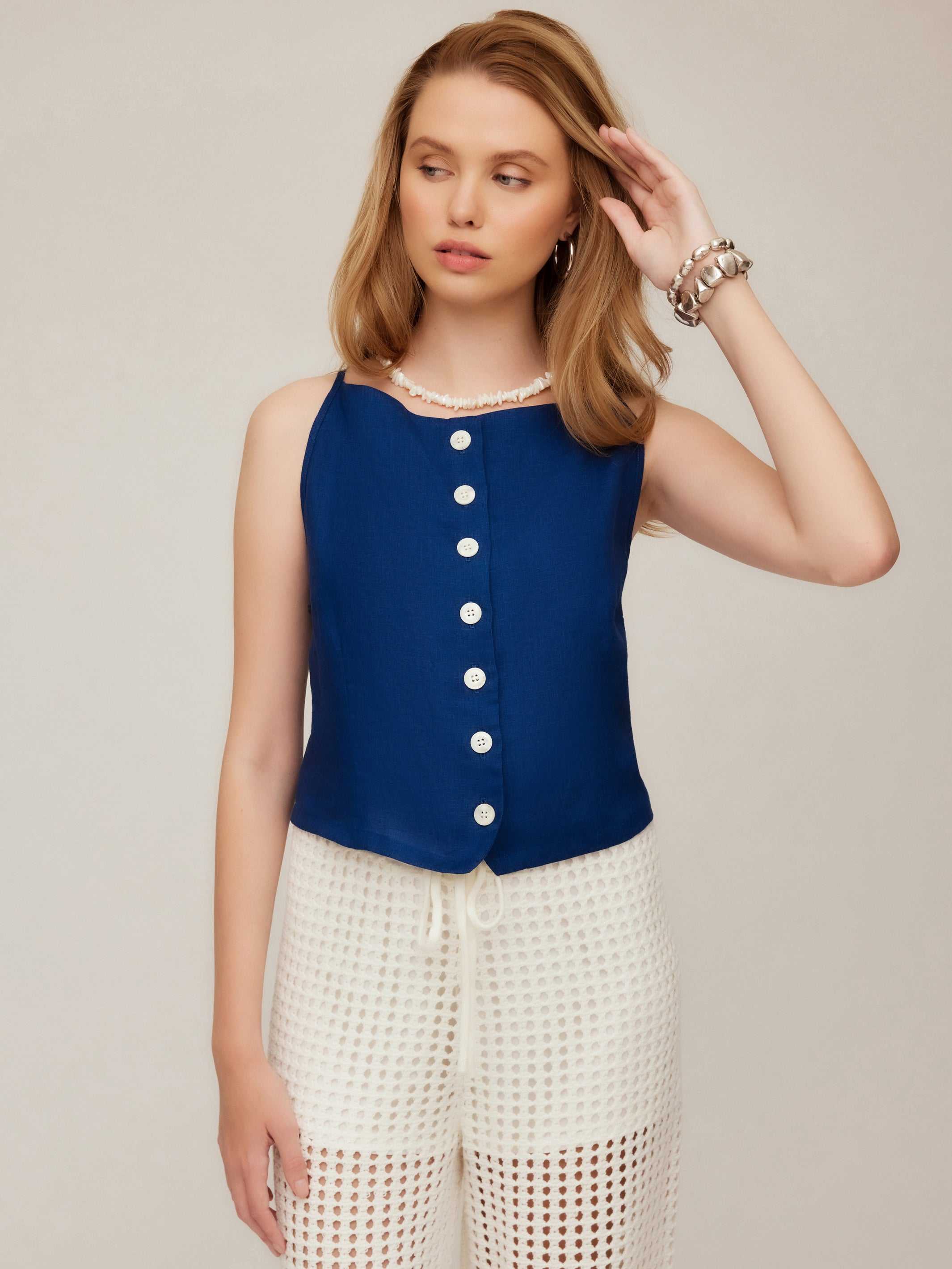 Woman wearing a navy Elis Sleeveless Button-Up Top with white buttons and white crochet shorts.