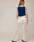 Woman wearing a navy Elis Sleeveless Button-Up Top with boxy fit and white crochet wide-leg pants, back view.