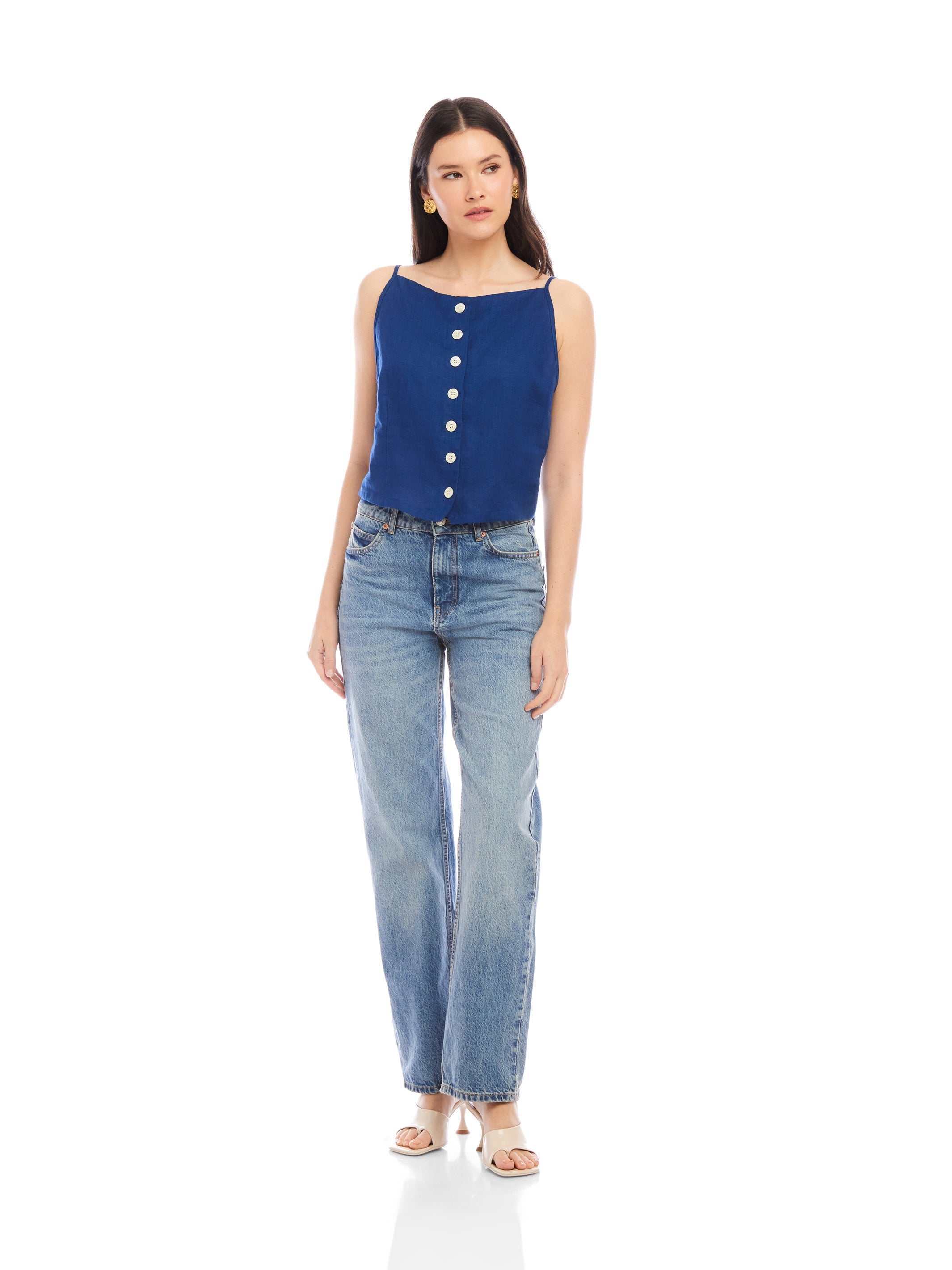 Woman wearing a navy Elis sleeveless button-up top with functional buttons and boat neck paired with light blue jeans and white sandals